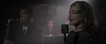 Movie still from “Yves Saint Laurent” (2014), directed by Jalil Lespert – A man and a woman singing into a microphone in a room; Medium shot, Over the shoulder angle