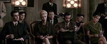 Movie still from “Yves Saint Laurent” (2014), directed by Jalil Lespert – A woman sitting in a chair next to a man in a suit and tie; Medium shot, Low angle