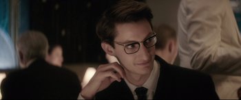Movie still from “Yves Saint Laurent” (2014), directed by Jalil Lespert – A man in a suit and glasses is looking at the camera; Close Up shot, Over the shoulder angle