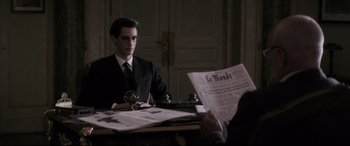 Movie still from “Yves Saint Laurent” (2014), directed by Jalil Lespert – A man sitting at a table reading a newspaper; Medium shot, Over the shoulder angle