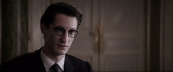 Movie still from “Yves Saint Laurent” (2014), directed by Jalil Lespert – A person wearing glasses and a suit; Close Up shot, Over the shoulder angle