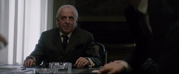 Movie still from “Yves Saint Laurent” (2014), directed by Jalil Lespert – An older man sitting at a table in front of another man in a suit; Medium shot, Over the shoulder angle