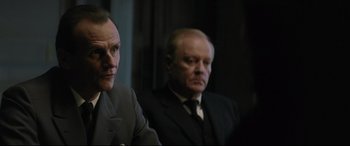 Movie still from “Yves Saint Laurent” (2014), directed by Jalil Lespert – Two men in suits sitting next to each other in a dark room; Close Up shot, Over the shoulder angle