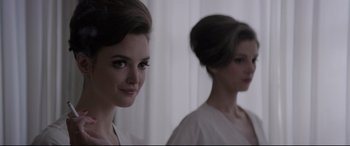Movie still from “Yves Saint Laurent” (2014), directed by Jalil Lespert – A woman with a bun and a white dress is reflected in a mirror; Close Up shot, Over the shoulder angle