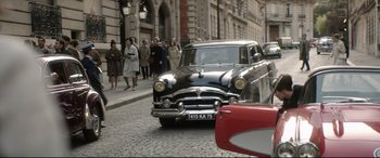 Movie still from “Yves Saint Laurent” (2014), directed by Jalil Lespert – An old car is parked on the side of the street; Wide shot, High angle