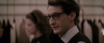 Movie still from “Yves Saint Laurent” (2014), directed by Jalil Lespert – A young man wearing glasses and a black suit; Close Up shot, Over the shoulder angle
