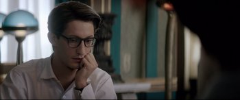 Movie still from “Yves Saint Laurent” (2014), directed by Jalil Lespert – A man with glasses is sitting in front of a lamp; Close Up shot, Low angle