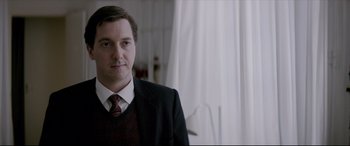 Movie still from “Yves Saint Laurent” (2014), directed by Jalil Lespert – A man in a suit and tie standing in front of a window; Close Up shot, Over the shoulder angle