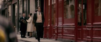 Movie still from “Yves Saint Laurent” (2014), directed by Jalil Lespert – A man walking down the street in front of a building; Wide shot, Over the shoulder angle