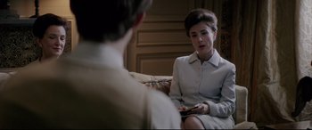 Movie still from “Yves Saint Laurent” (2014), directed by Jalil Lespert – A woman sitting in front of a man holding a cell phone; Medium shot, Over the shoulder angle
