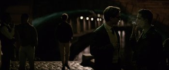 Movie still from “Yves Saint Laurent” (2014), directed by Jalil Lespert – A man standing next to another man in a dark room; Medium shot, Over the shoulder angle