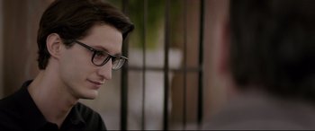 Movie still from “Yves Saint Laurent” (2014), directed by Jalil Lespert – A young man wearing glasses and a black shirt; Close Up shot, Over the shoulder angle