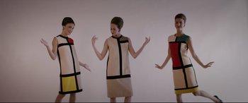 Movie still from “Yves Saint Laurent” (2014), directed by Jalil Lespert – A group of three women wearing dresses and standing in front of a white wall; Medium shot, Overhead angle