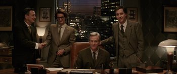 Movie still from “Yves Saint Laurent” (2014), directed by Jalil Lespert – A group of men standing around a table; Medium shot, High angle