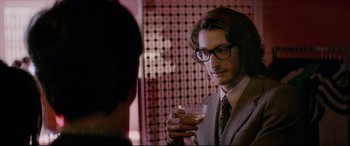 Movie still from “Yves Saint Laurent” (2014), directed by Jalil Lespert – A man in a suit holding a glass of wine; Close Up shot, Over the shoulder angle