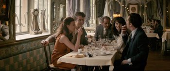 Movie still from “Yves Saint Laurent” (2014), directed by Jalil Lespert – A group of people sitting at a table with wine glasses; Medium shot, Over the shoulder angle