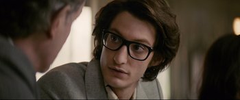 Movie still from “Yves Saint Laurent” (2014), directed by Jalil Lespert – A young man wearing glasses and a suit; Close Up shot, Over the shoulder angle