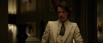 Movie still from “Yves Saint Laurent” (2014), directed by Jalil Lespert – A man in a suit and tie standing in a room; Medium shot, Over the shoulder angle