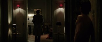 Movie still from “Yves Saint Laurent” (2014), directed by Jalil Lespert – A person standing in a room with a lamp on; Wide shot, Over the shoulder angle