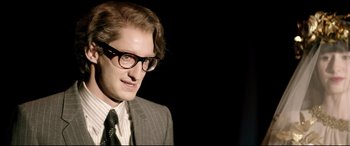 Movie still from “Yves Saint Laurent” (2014), directed by Jalil Lespert – A man in a suit and tie wearing glasses; Close Up shot, Over the shoulder angle