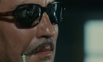 Movie still from “Z” (1969), directed by Costa-Gavras – A man wearing sunglasses and holding a cigarette; Extreme Close Up shot, Low angle