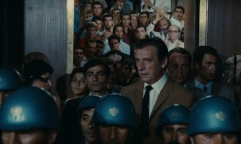 Movie still from “Z” (1969), directed by Costa-Gavras – A group of people standing in front of a wall; Medium shot, Over the shoulder angle