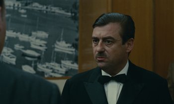 Movie still from “Z” (1969), directed by Costa-Gavras – A person wearing a suit and tie; Close Up shot, Over the shoulder angle