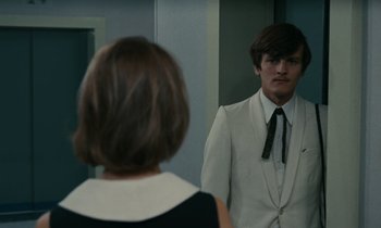 Movie still from “Z” (1969), directed by Costa-Gavras – A man in a white suit is looking at a woman in a black dress; Medium shot, Over the shoulder angle
