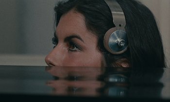 Movie still from “Z” (1969), directed by Costa-Gavras – A woman wearing headphones looking over her shoulder; Close Up shot, Overhead angle