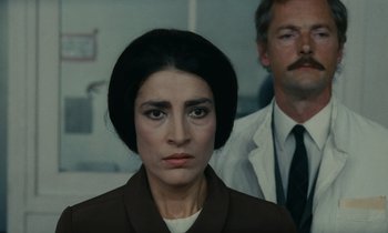 Movie still from “Z” (1969), directed by Costa-Gavras – A woman in a brown jacket standing next to a man in a white suit; Close Up shot, Low angle