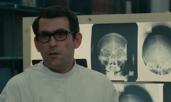 Movie still from “Z” (1969), directed by Costa-Gavras – A man wearing glasses and a white shirt is in front of an x - ray; Close Up shot, Low angle