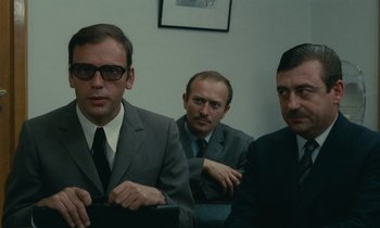 Movie still from “Z” (1969), directed by Costa-Gavras – A group of men sitting next to each other in a room; Medium shot, Over the shoulder angle