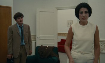 Movie still from “Z” (1969), directed by Costa-Gavras – A man and a woman standing in front of a couch; Medium shot, Low angle