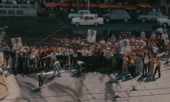 Movie still from “Z” (1969), directed by Costa-Gavras – A group of people standing around a crowd of onlookers; Extreme Wide shot, High angle