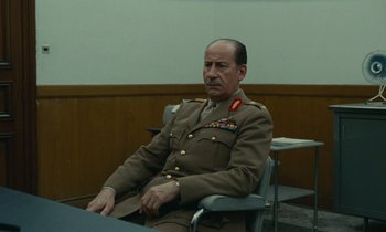 Movie still from “Z” (1969), directed by Costa-Gavras – A man in a military uniform sitting in a chair; Medium shot, Over the shoulder angle