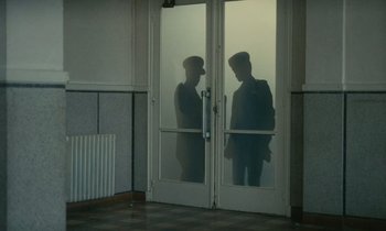 Movie still from “Z” (1969), directed by Costa-Gavras – Two men standing in front of each other in front of a door; Wide shot, Low angle