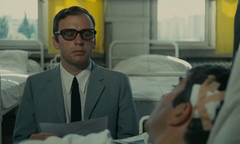 Movie still from “Z” (1969), directed by Costa-Gavras – A man wearing a suit and tie sitting at a table; Close Up shot, Over the shoulder angle