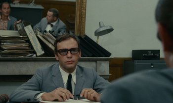 Movie still from “Z” (1969), directed by Costa-Gavras – A man sitting at a desk in front of a mirror; Medium shot, Over the shoulder angle