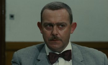 Movie still from “Z” (1969), directed by Costa-Gavras – A person wearing a suit and a bow tie; Close Up shot, Over the shoulder angle