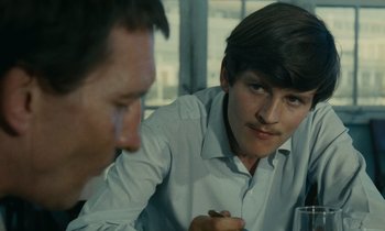 Movie still from “Z” (1969), directed by Costa-Gavras – A man sitting at a table with another man in front of him; Close Up shot, Over the shoulder angle