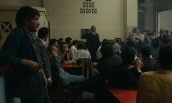 Movie still from “Z” (1969), directed by Costa-Gavras – A group of people sitting in a room; Wide shot, Over the shoulder angle