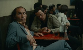 Movie still from “Z” (1969), directed by Costa-Gavras – A man sitting at a table with a bottle of alcohol; Medium shot, High angle