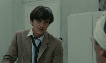 Movie still from “Z” (1969), directed by Costa-Gavras – A man in a suit and tie in front of a wall; Close Up shot, Low angle