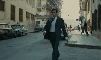 Movie still from “Z” (1969), directed by Costa-Gavras – A man walking down the street in a suit and tie; Wide shot, Low angle