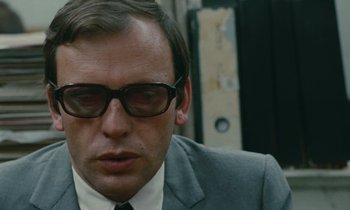 Movie still from “Z” (1969), directed by Costa-Gavras – A person wearing a suit and glasses; Close Up shot, Low angle