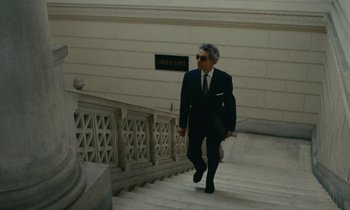 Movie still from “Z” (1969), directed by Costa-Gavras – A man in a suit walking down the stairs; Wide shot, Low angle