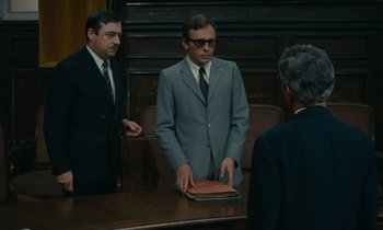 Movie still from “Z” (1969), directed by Costa-Gavras – A man in a suit and tie standing in front of two other men; Medium shot, Low angle