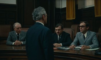 Movie still from “Z” (1969), directed by Costa-Gavras – A group of men sitting at a table in a room; Wide shot, Over the shoulder angle