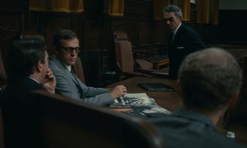Movie still from “Z” (1969), directed by Costa-Gavras – A man sitting at a table in front of two other men; Medium shot, Over the shoulder angle