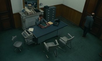 Movie still from “Z” (1969), directed by Costa-Gavras – A man sitting at a desk in an office setting; Wide shot, High angle